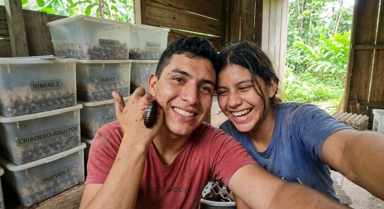 Two members of the farm team taking a selfie with a Blaberus giganteus cockroach resting on a shoulder